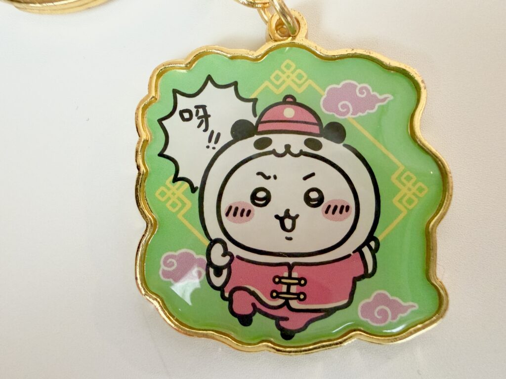 パンダの衣装を着て中国風の服装でポーズを取るハチワレのキーホルダー