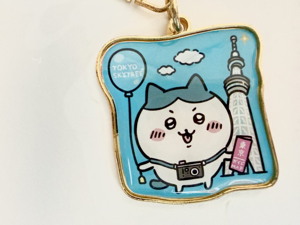 東京スカイツリーの前でカメラを持つハチワレのキーホルダー